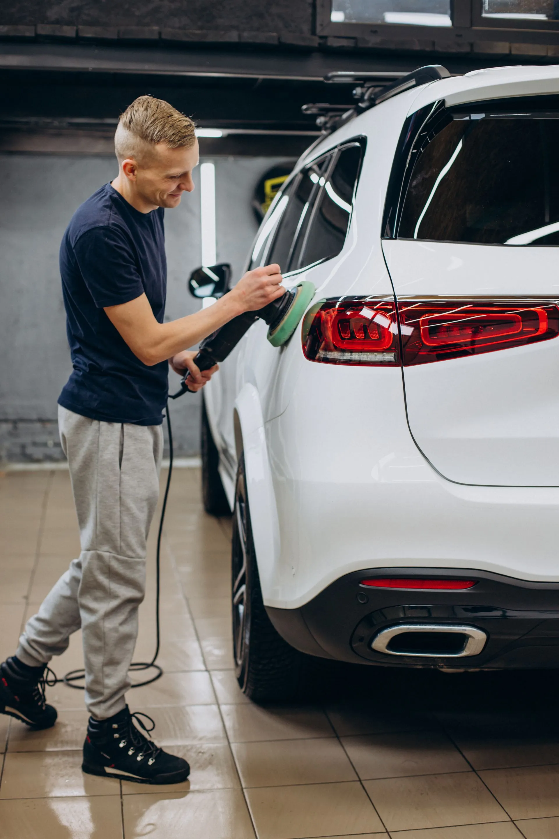 Man polishing a white SUV with a machine in a garage.