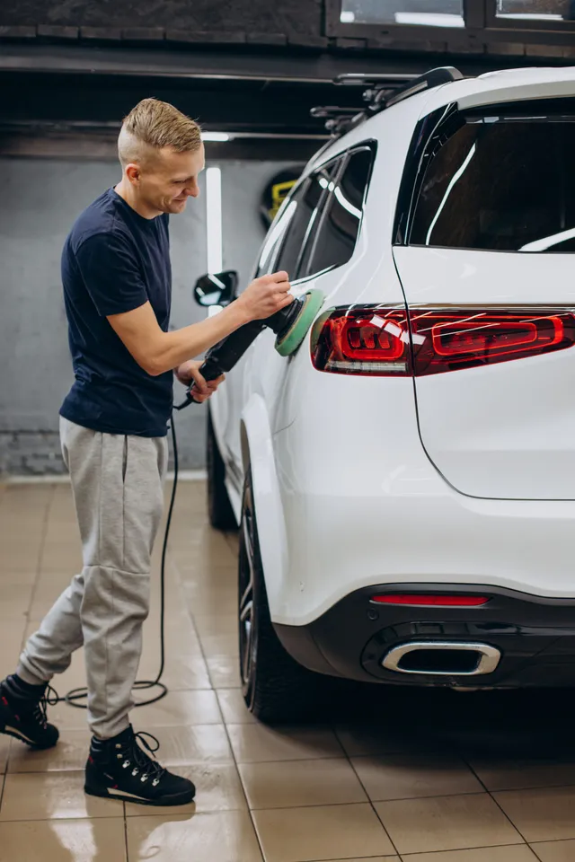 Man polishing a white SUV with a machine in a garage.