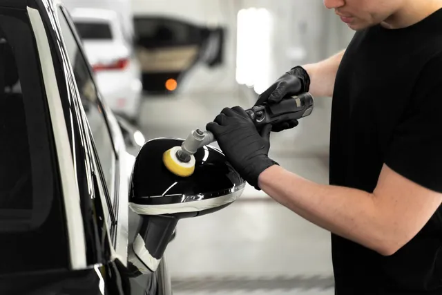 Person applying car wax with a blue applicator to a gray car door.