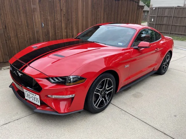 Red Ford Mustang with black racing stripes parked on a driveway.