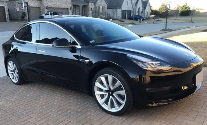 Black Tesla Model 3 parked on a brick driveway in front of a house.