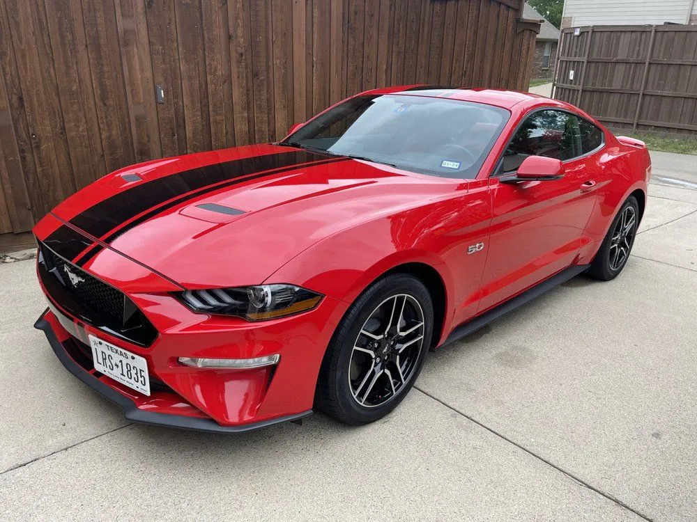 Red Ford Mustang coupe with black racing stripes parked on a concrete driveway.